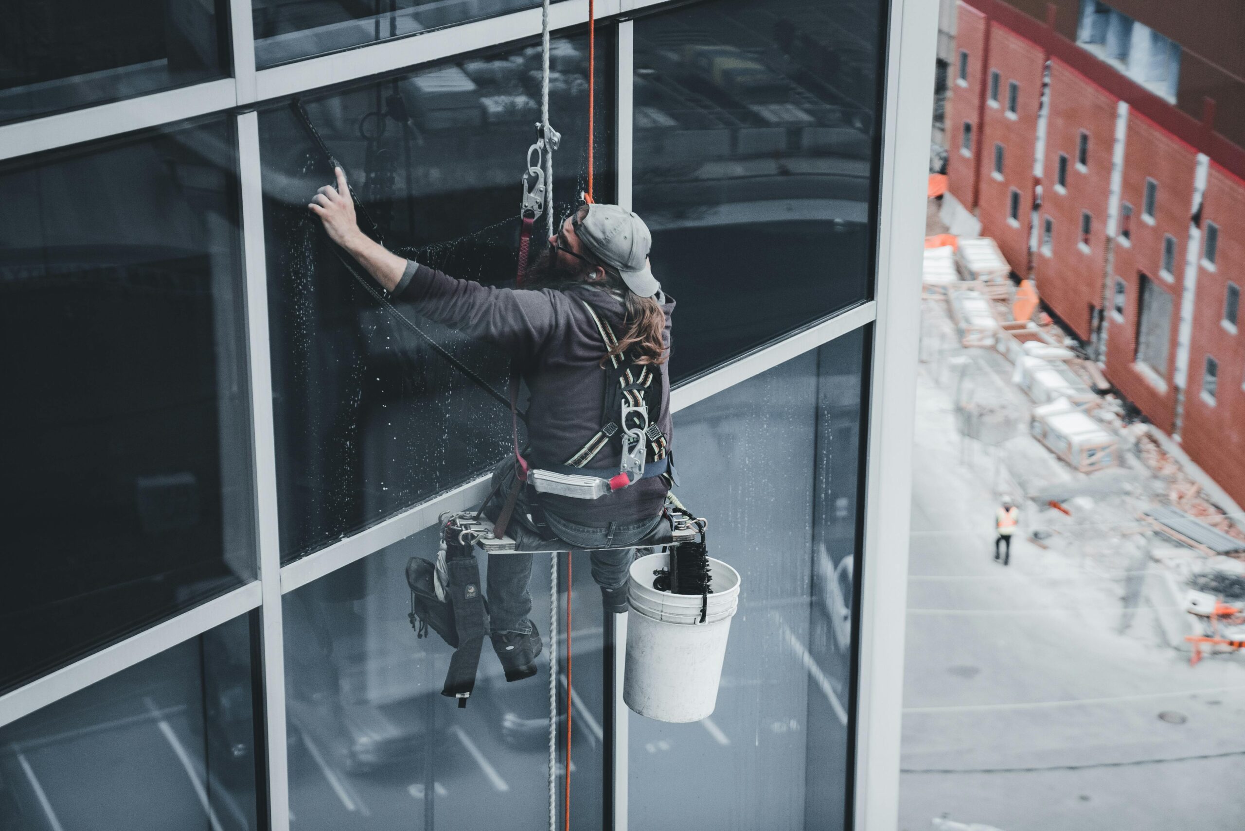 A worker cleaning skyscraper windows with a harness in an urban setting.