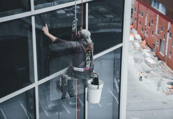 A worker cleaning skyscraper windows with a harness in an urban setting.